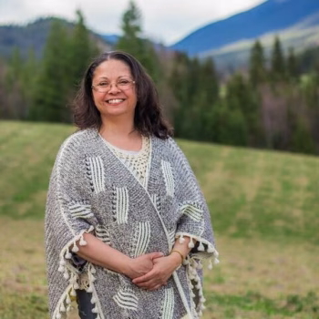 Jennifer Regular smiling outdoors with mountains in the background, wearing a patterned poncho.